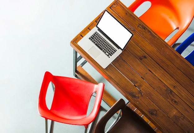 Eine Draufsicht eines offenen Laptops auf Holztisch mit bunten Stühlen