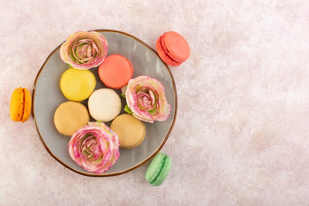 Eine Draufsicht färbte französische Macarons mit Blumen innerhalb Platte auf dem rosa Schreibtischkuchen-Kekszuckersüß