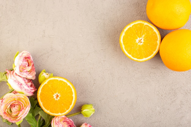 Eine Draufsicht frische Orangen sauer reif geschnitten und ganze milde Zitrus tropische Vitamin gelb zusammen mit getrockneten Blumen auf dem cremefarbenen Schreibtisch