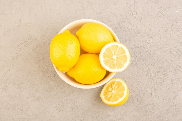 Eine Draufsicht frische Zitronen sauer reif ganze milde Zitrus tropisches Vitamin gelb zusammen mit getrockneten Blumen auf dem cremefarbenen Schreibtisch