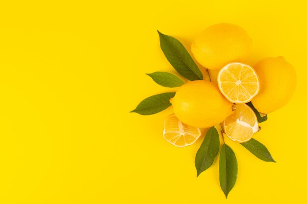 Eine Draufsicht gelbe frische Zitronen frisch reif ganz und geschnitten zusammen mit grünen Blättern Früchte isoliert auf der gelben Hintergrund Zitrusfrucht Farbe