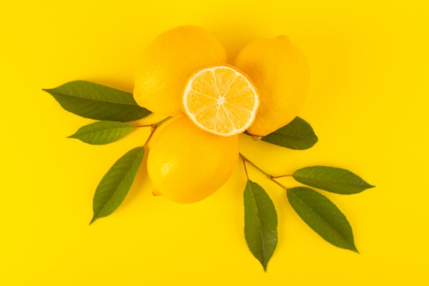 Eine Draufsicht gelbe frische Zitronen frisch reif ganz und geschnitten zusammen mit grünen Blättern Früchte isoliert auf der gelben Hintergrund Zitrusfrucht Farbe