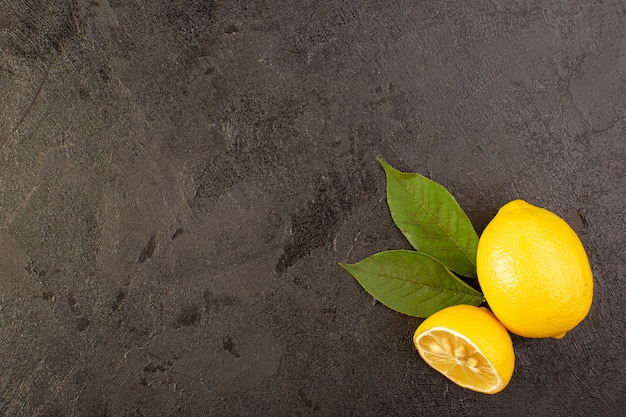 Eine Draufsicht gelbe frische Zitronen weich und saftig ganz und geschnitten mit grünen Blättern auf dem dunklen Hintergrund Früchte Zitrusfarbe