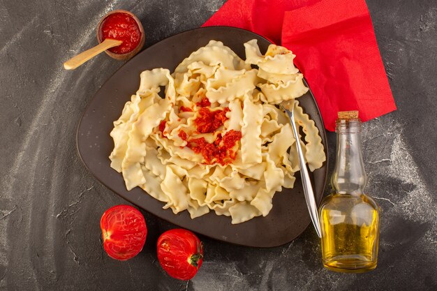Eine Draufsicht kochte italienische Nudeln mit Tomatensauce innerhalb Platte auf dem grauen Tisch Essen Mahlzeit italienische Nudeln