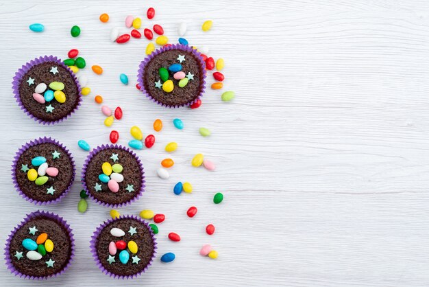 Eine Draufsicht köstliche Brownies innerhalb lila Formen mit bunten Bonbons auf weißen, bonbonfarbenen Süßigkeiten