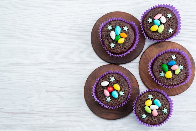 Eine Draufsicht köstliche Brownies innerhalb lila Formen mit bunten Bonbons auf weißen, bonbonfarbenen Süßigkeiten