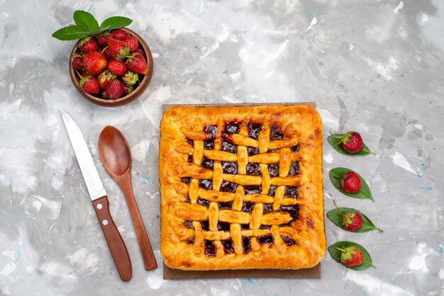 Eine Draufsicht köstlicher Erdbeerkuchen mit Erdbeergelee nach innen zusammen mit frischen Erdbeeren auf dem grauen Schreibtischkuchen