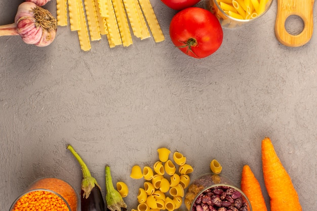 Eine Draufsicht rohe Nudeln gelb trockene lange italienische Nudeln zusammen mit roten Tomaten Auberginen Karotten und Knoblauch isoliert auf dem grauen Hintergrund Gemüse Lebensmittel Mahlzeit