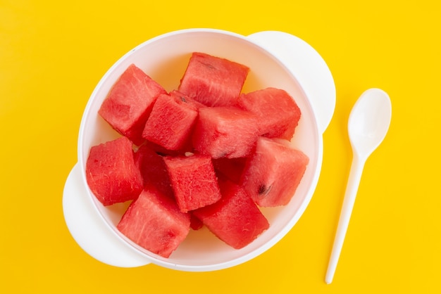 Eine Draufsicht schnitt frische Wassermelone in weiße Plastikteller auf gelbem Schreibtisch, Fruchtsommerfarbe