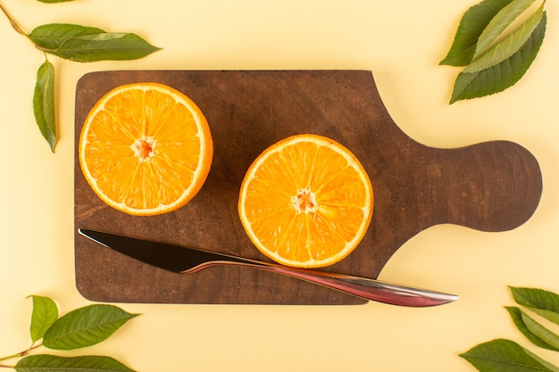 Eine Draufsicht schnitt ganze Orange frisch saftig weich zusammen mit silbernem Messer und grünen Blättern auf dem braunen Holzschreibtisch und cremefarbenem Hintergrund Zitrusorange
