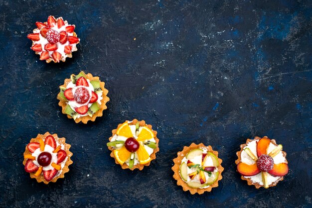 Eine Draufsicht verschiedene kleine Kuchen mit Sahne und frisch geschnittenen Früchten auf dem blauen Hintergrund