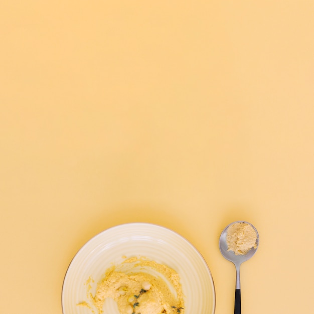 Kostenloses Foto eine draufsicht von selbst gemachtem hummus auf platte und löffel gegen beige hintergrund