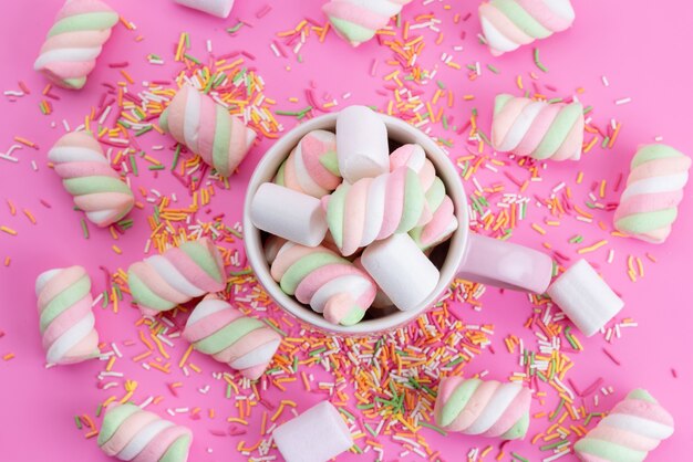 Eine Draufsicht weiß-rosa Marshmallows süß und klebrig zusammen mit bunten Bonbonpartikeln auf rosa