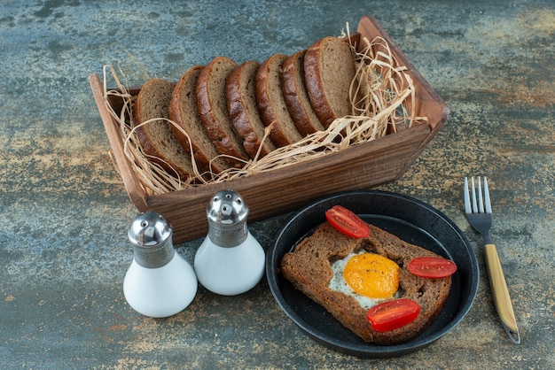 Eine dunkle Pfanne mit Spiegelei und Scheiben Schwarzbrot auf Marmorhintergrund