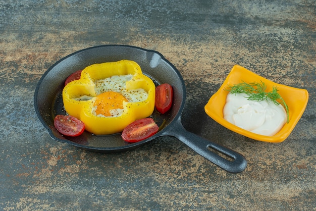 Eine dunkle Pfanne mit Spiegelei und Tomaten- und Sauerrahm auf Marmorhintergrund