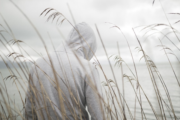 Eine einsame traurige Person von hinten mit einem Kapuzenpulli, der in der Nähe des Meeres sitzt und über das Leben nachdenkt