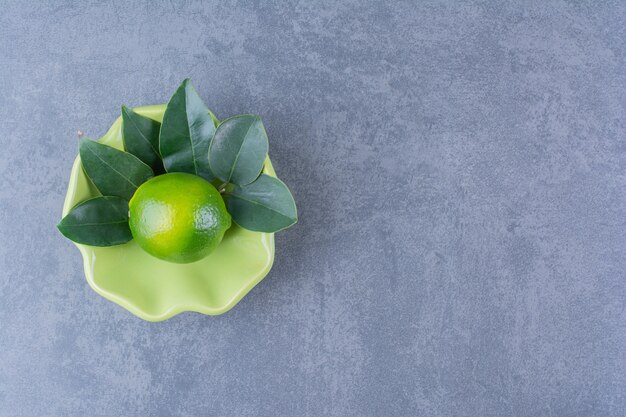 Eine einzelne Zitrone mit Blättern in der Schüssel auf Marmortisch.