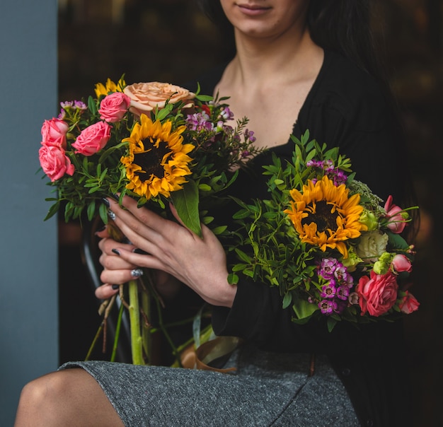 Eine elegante Frau, die Blumenstrauß zwei der Rosen und der Sonnenblumen anhält