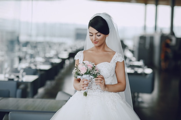 Eine elegante und schöne Braut in einem weißen Kleid und in einem Schleier, die mit Blumenstrauß von Blumen stehen