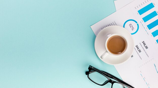 Eine erhöhte Ansicht der Kaffeetasse auf Geschäftsbudgetplan und -brillen auf blauem Hintergrund