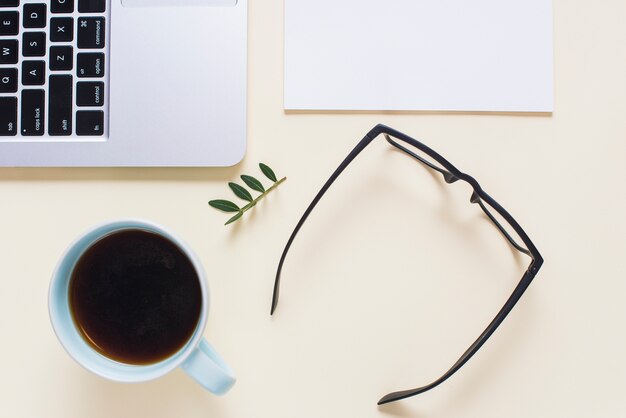 Eine erhöhte Ansicht der schwarzen Brille; Teetasse; Laptop und Papier auf beige Hintergrund