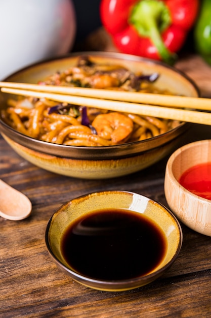 Eine erhöhte Ansicht der thailändischen Udon-Nudel mit Essstäbchen und Sojasoße auf Holztisch