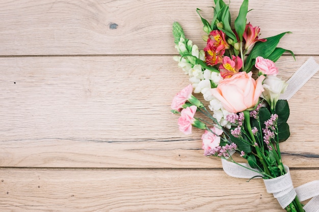 Eine erhöhte Ansicht des bunten Blumenblumenstraußes gebunden mit weißem Band auf hölzernem Schreibtisch