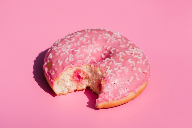 Eine erhöhte Ansicht des gegessenen Donuts auf rosa Hintergrund