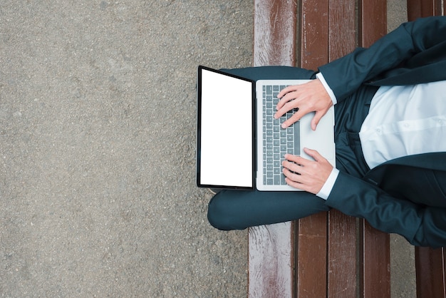 Eine erhöhte Ansicht des Geschäftsmannes sitzend auf der Bank, die auf Laptop schreibt