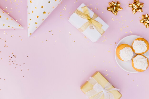 Eine erhöhte Ansicht des Partyhutes; Geschenkbox; Bogen und Cupcake mit Konfetti auf rosa Hintergrund