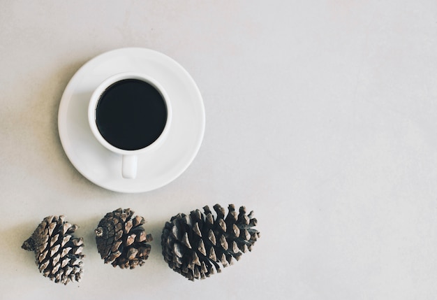 Eine erhöhte Ansicht von Kiefernkegeln und von Kaffeetasse und Untertasse auf weißem Hintergrund