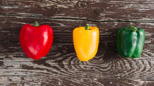 Eine erhöhte Ansicht von Rot; gelbe und grüne Paprika auf beschädigter Holzoberfläche