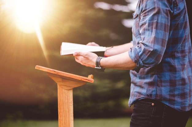 Eine flache Fokusaufnahme eines Mannes, der die Bibel liest, während er in der Nähe eines Podiums steht