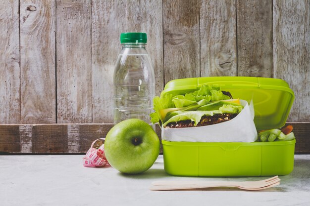 Eine Flasche Wasser und Apfel neben einer Lunchbox