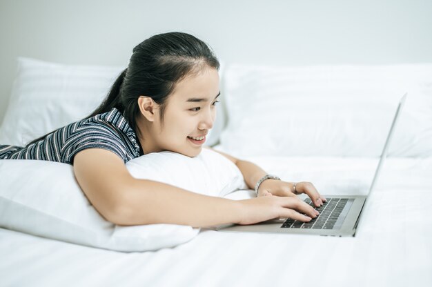 Eine Frau, die ein gestreiftes Hemd auf dem Bett trägt und einen Laptop spielt.