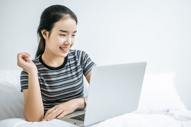 Eine Frau, die ein gestreiftes Hemd auf dem Bett trägt und glücklich Laptop spielt.