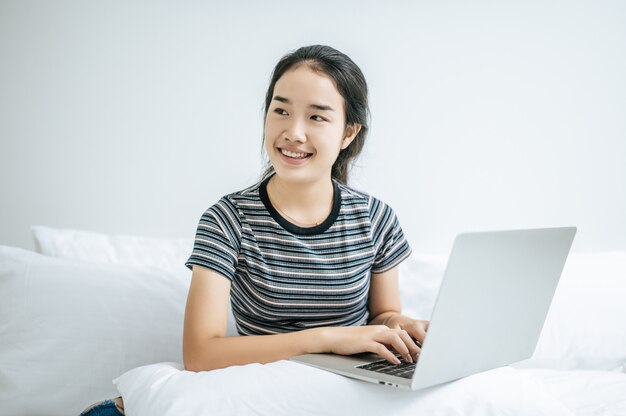 Eine Frau, die ein gestreiftes Hemd auf dem Bett trägt und glücklich Laptop spielt.