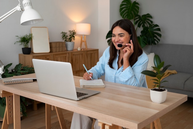 Kostenloses Foto eine frau, die zu hause einen videoanruf auf einem laptop mit headset macht