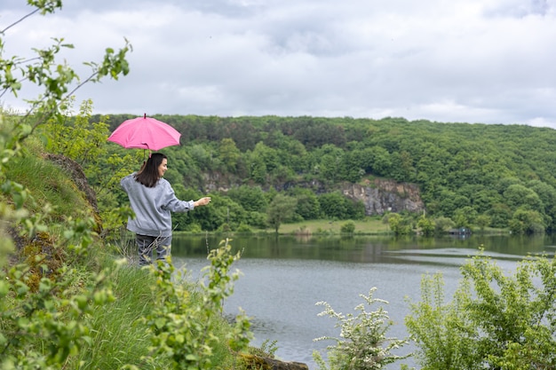 Eine Frau geht bei bewölktem Wetter unter einem Regenschirm in einer bergigen Gegend spazieren