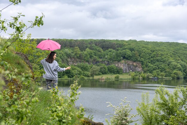 Eine Frau geht bei bewölktem Wetter unter einem Regenschirm in einer bergigen Gegend spazieren