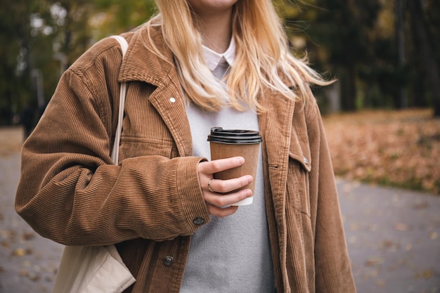 Eine Frau hält bei einem Spaziergang im Park ein Einwegglas Kaffee in der Hand