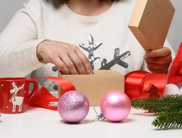 Eine frau im weißen pullover sitzt am tisch und verpackt geschenke zu weihnachten. vorbereitung auf die feiertage