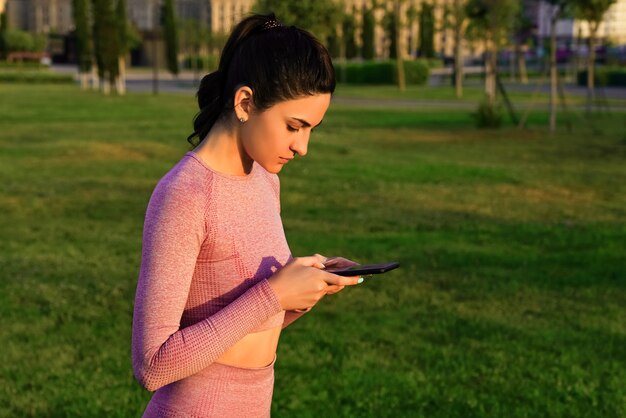 Eine Frau im Yoga-Anzug macht es am frühen Morgen mit einem Telefon in der Hand im Morgengrauen.