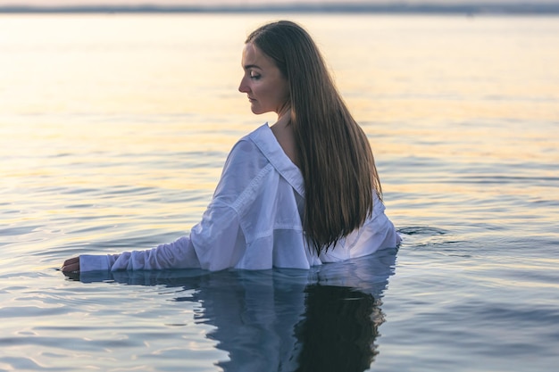 Eine Frau in einem Badeanzug und einem weißen Hemd im Meer bei Sonnenuntergang