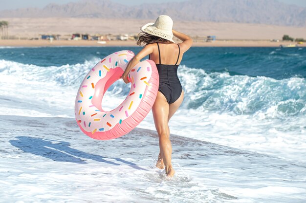 Eine Frau in einem Hut mit einem donutförmigen Schwimmkreis am Meer. Das Konzept von Freizeit und Unterhaltung im Urlaub.