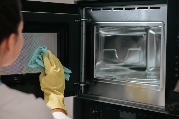 Eine Frau in gelben Handschuhen, die den Ofen putzt