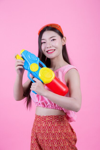 Eine Frau kleidete in der traditionellen thailändischen Volkskleidung an, die einen Wasserwerfer auf einem rosa Hintergrund hält.