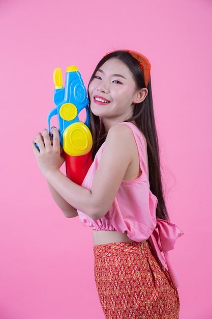 Eine Frau kleidete in der traditionellen thailändischen Volkskleidung an, die einen Wasserwerfer auf einem rosa Hintergrund hält.