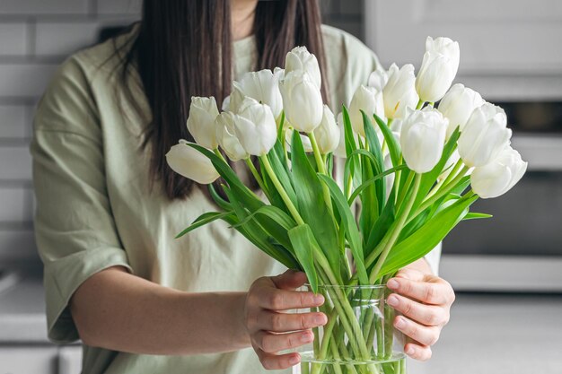 Eine Frau legt ein Bouquet weißer Tulpenblumen in eine Vase in der Küche