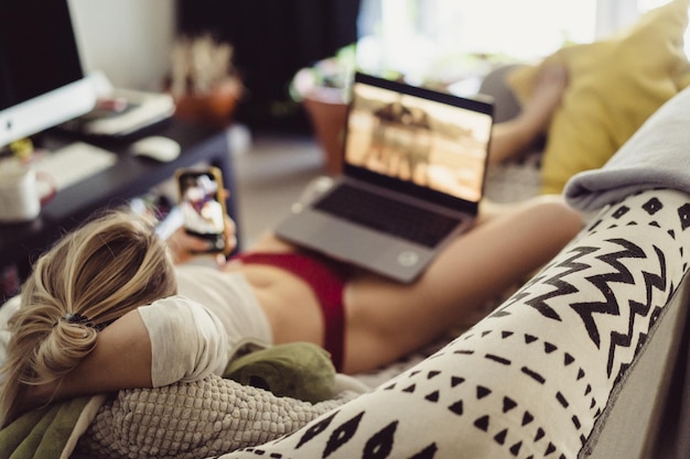 Kostenloses Foto eine frau liegt mit einem laptop auf einem sofa. freizeit auf isolation. arbeiten am laptop von zu hause aus.